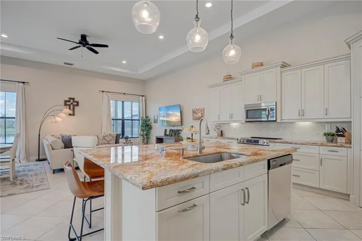 Kitchen with open floor plan, a breakfast bar, white cabinets, light stone countertops, and light tile patterned floors