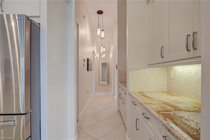 Kitchen with freestanding refrigerator, light stone counters, light tile patterned flooring, backsplash, and white cabinetry