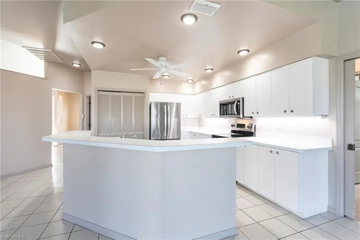 Kitchen with stainless steel appliances, light tile patterned flooring, a kitchen island with sink, and white cabinets.
