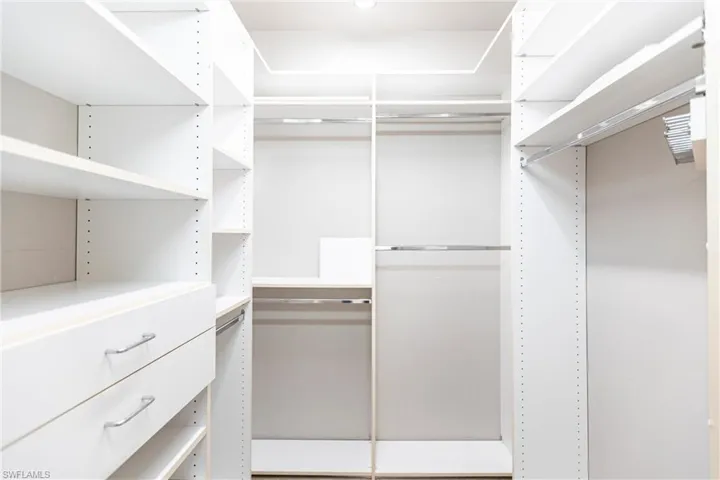 View of spacious custom (Closets-by-Design) neutral carpeted closet with two drawers and adjustable shelving and racks.