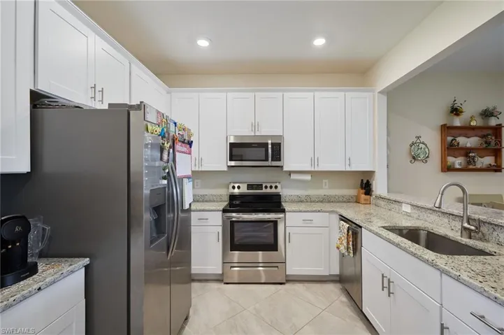 Kitchen featuring white cabinetry, sink, light stone countertops, and appliances with stainless steel finishes