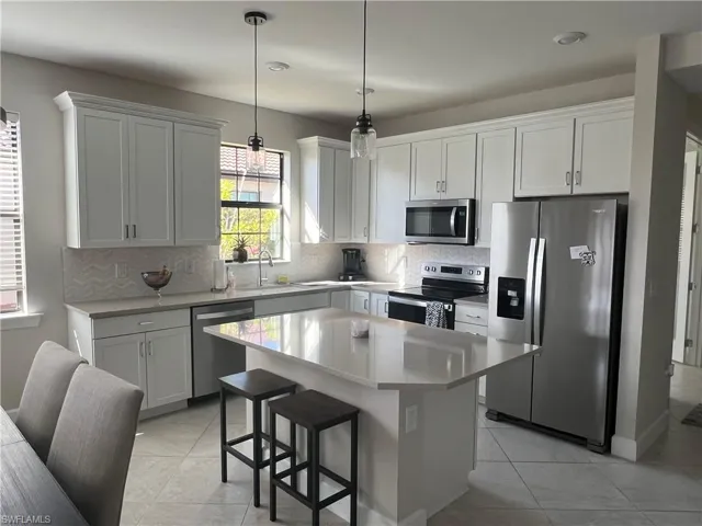 Kitchen with stainless steel appliances, a kitchen island, a breakfast bar, and white cabinetry