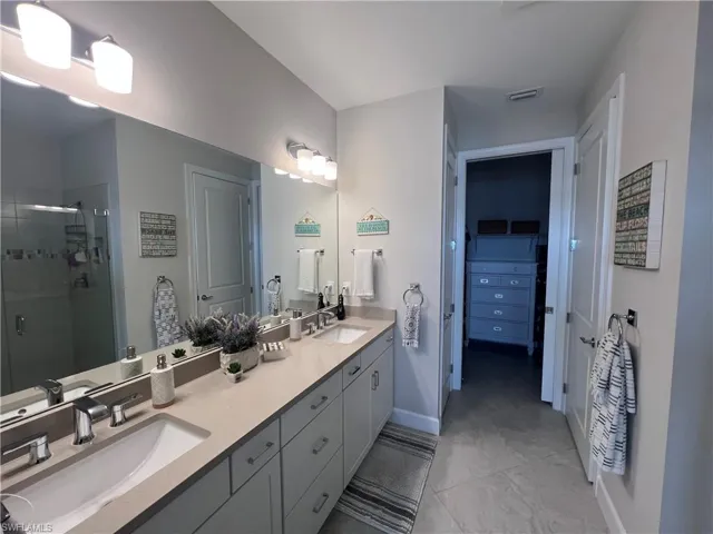 Full bath featuring double vanity, a stall shower, and a spacious closet