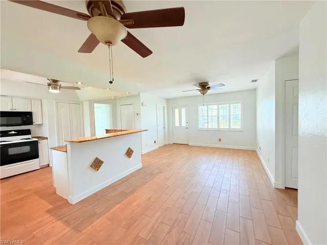 Kitchen with white range with electric cooktop, white cabinets, light wood-style floors, black microwave, and a center island