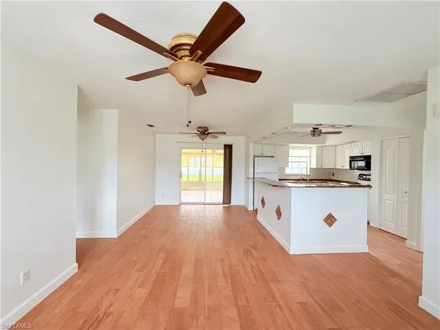 Kitchen featuring white cabinetry, dark countertops, light wood finished floors, black microwave, and open floor plan