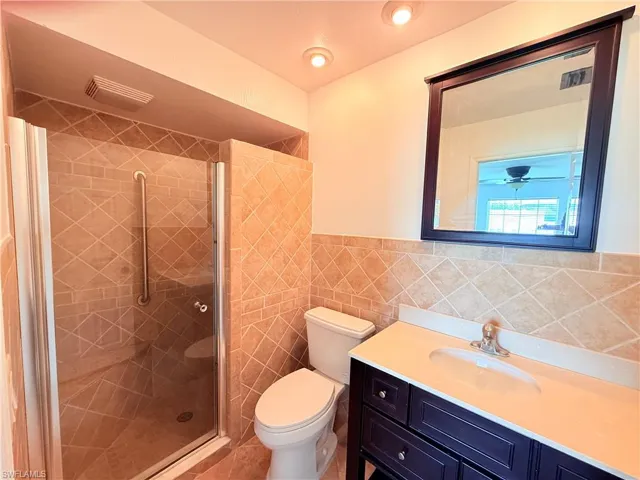 Full bath with a stall shower, vanity, and tile walls