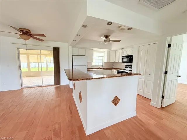 Kitchen featuring white appliances, light wood-style flooring, white cabinets, and ceiling fan