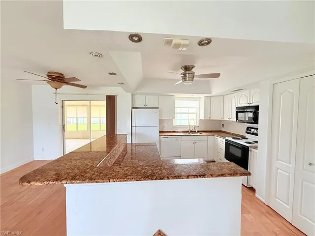 Kitchen with white appliances, white cabinetry, a tray ceiling, light wood finished floors, and a ceiling fan