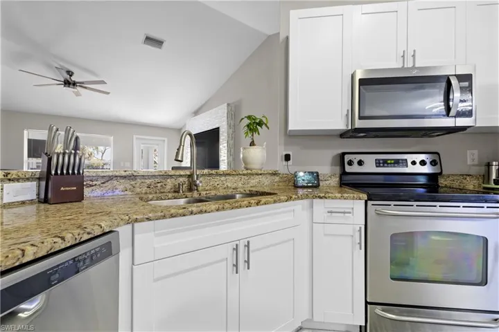 Kitchen with stainless steel appliances, a sink, lofted ceiling, light stone countertops, and white cabinetry