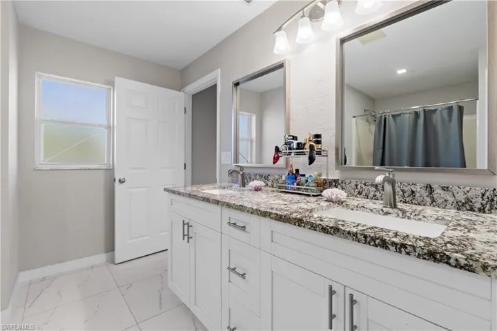 Bathroom with marble look tiles, double vanity, baseboards, and a shower with curtain