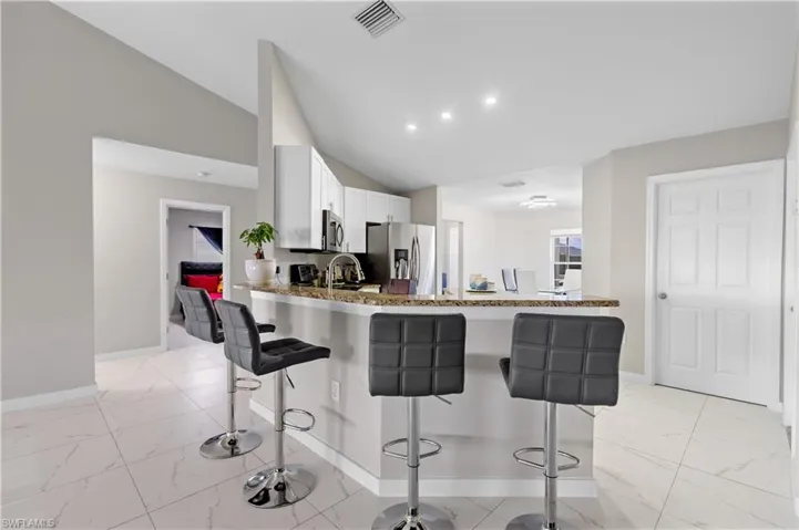 Kitchen with appliances with stainless steel finishes, light marble finish flooring, baseboards, a breakfast bar area, and vaulted ceiling