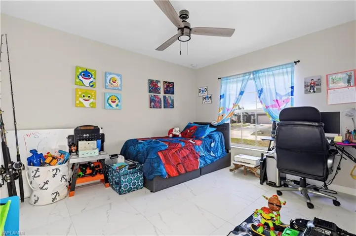 Bedroom with marble look tiles, an office area, and ceiling fan