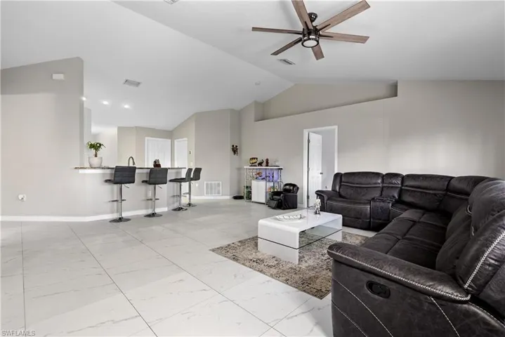 Living area featuring lofted ceiling, light marble finish flooring, ceiling fan, and baseboards