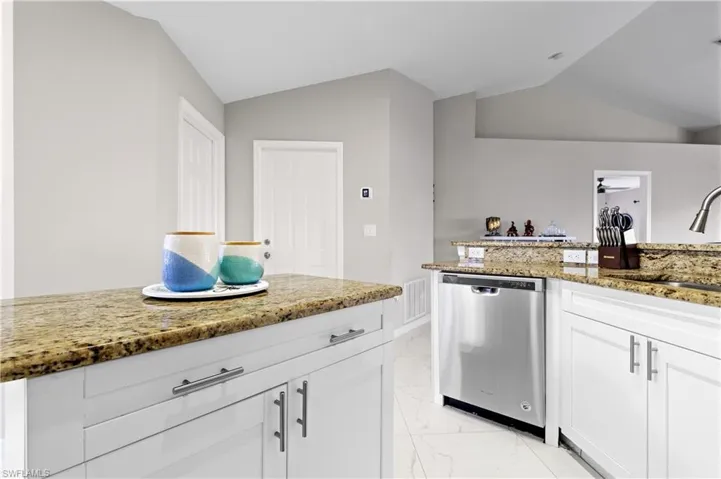 Kitchen with stainless steel dishwasher, light marble finish floors, a sink, lofted ceiling, and light stone countertops