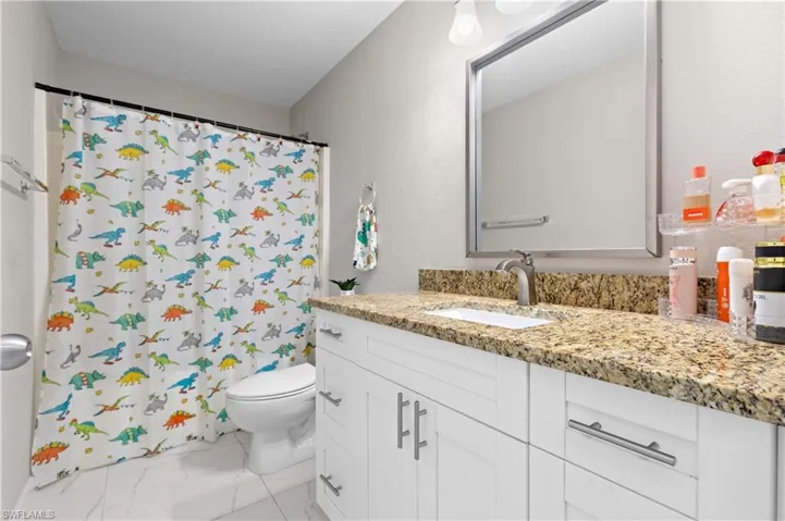 Bathroom with marble finish flooring, toilet, vanity, and a shower with shower curtain