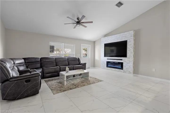 Living room featuring marble look tile flooring, a ceiling fan, vaulted ceiling, a stone fireplace, and baseboards