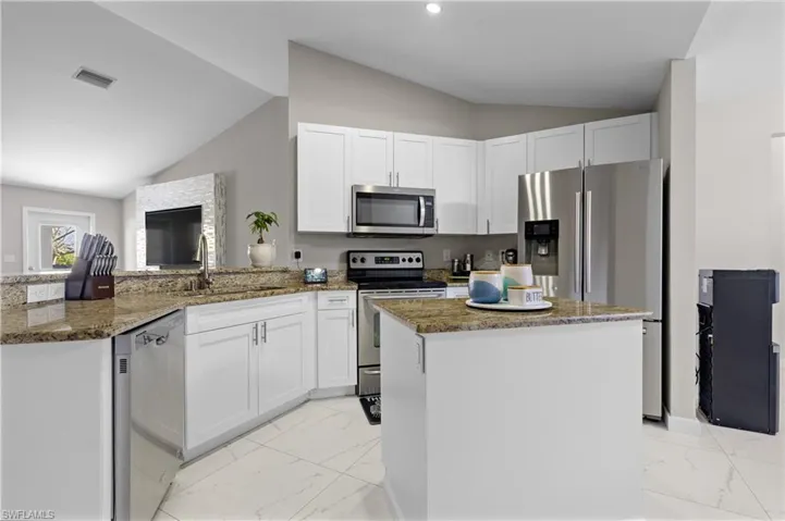 Kitchen featuring stainless steel appliances, lofted ceiling, a sink, light marble finish flooring, and a peninsula