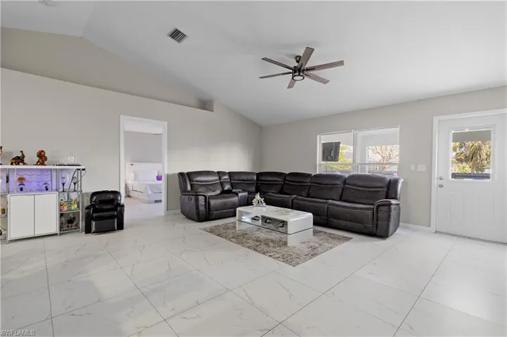 Living area with lofted ceiling, ceiling fan, marble look tile flooring, and baseboards