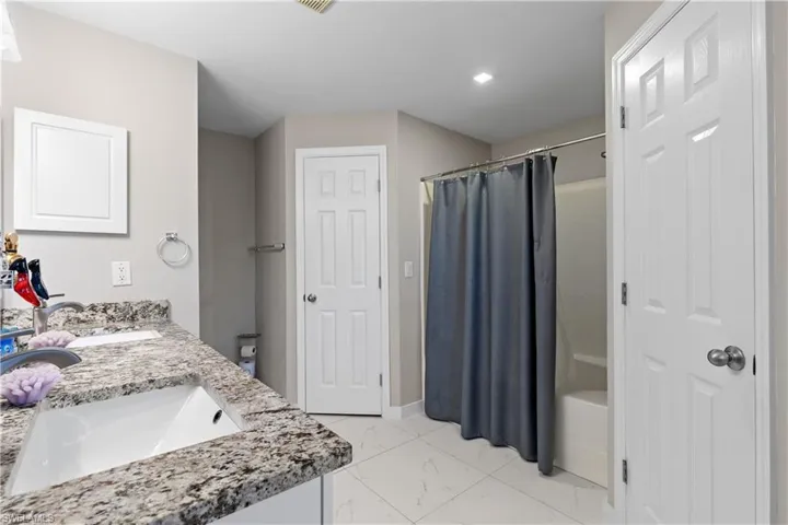 Bathroom featuring marble look tile flooring, curtained shower, double vanity, and recessed lighting