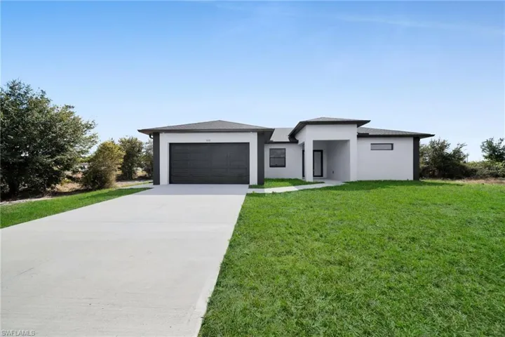 Prairie-style house with a front yard, stucco siding, driveway, a garage, and a shingled roof