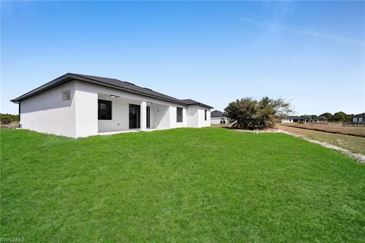 Rear view of property featuring a lawn, stucco siding, ceiling fan, and a patio