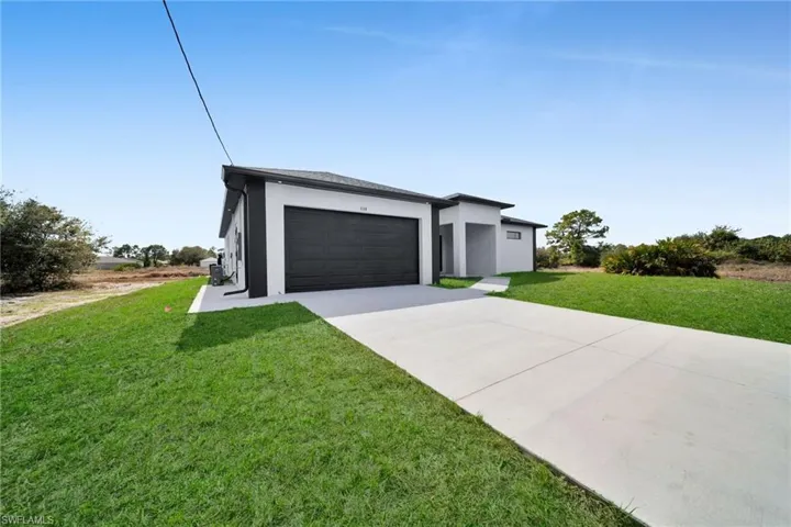 View of front facade featuring a front lawn, stucco siding, concrete driveway, and an attached garage
