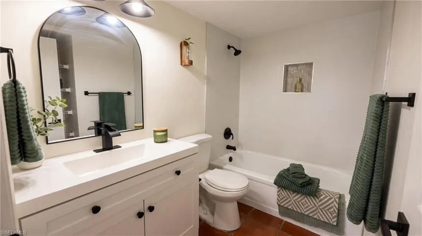 Bathroom featuring a white vanity with integrated sink, black hardware, arched mirror, and white bathtub with black fixtures