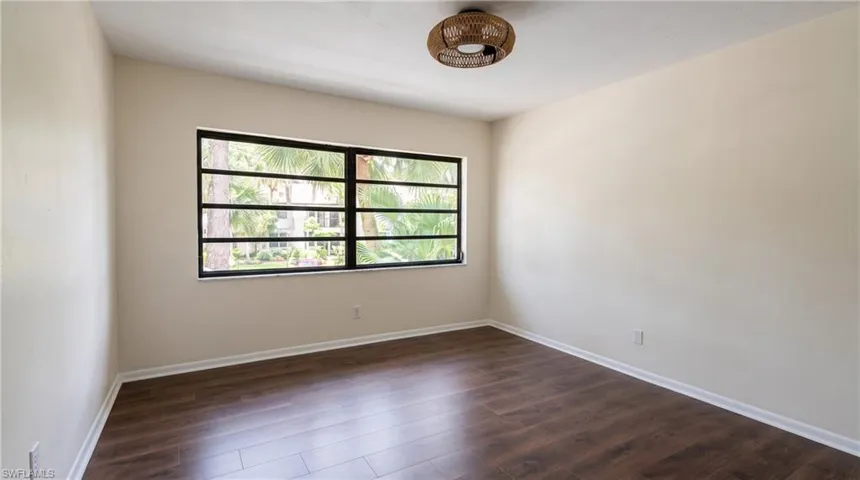 Spacious room featuring wood-finish flooring, neutral-toned walls, and a multi-pane window with black framing