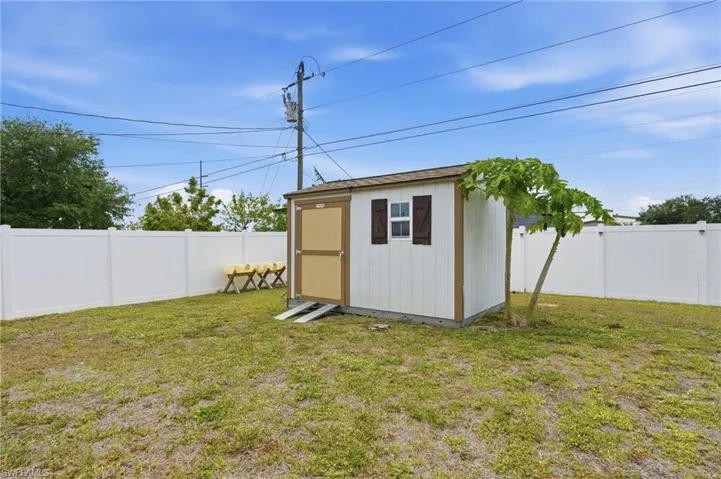 Backyard featuring a white vinyl privacy fence, a storage shed with a shingled roof, a single window with dark shutters, and a wood-finish door with metal screen
