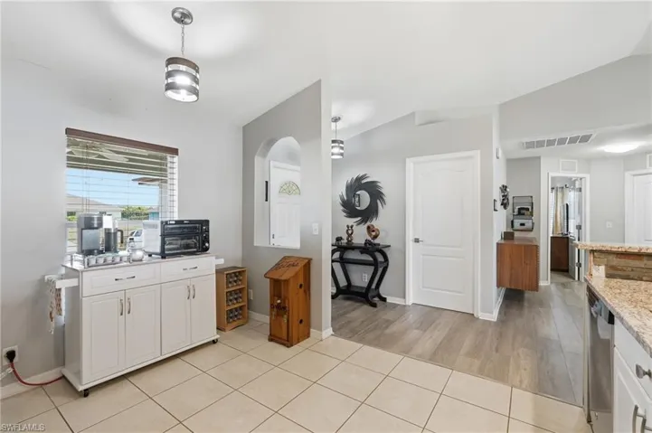 Tiled flooring transitions to wood-finish flooring in this interior space, featuring a window with horizontal blinds, an arched wall niche, and recessed lighting