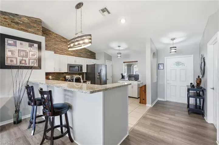 Kitchen featuring a breakfast bar with stone countertop, white cabinetry, integrated stainless steel appliances, and a stacked stone accent wall