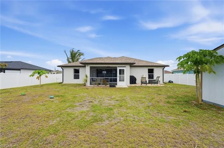 Expansive backyard featuring a white vinyl privacy fence, a covered screened lanai, an outdoor patio area, and mature tropical trees