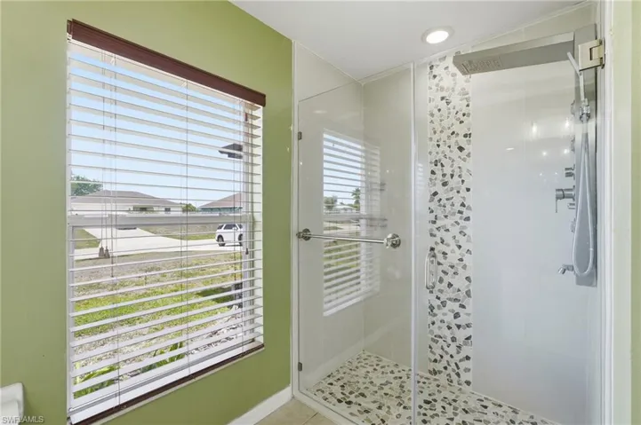 Walk-in shower featuring glass enclosure, pebble tile flooring, and a multi-function shower system