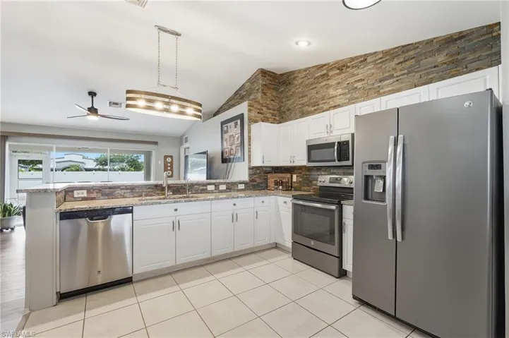 Well-appointed kitchen featuring white cabinetry, stainless steel appliances, granite countertops, a stacked stone accent wall, and tiled flooring