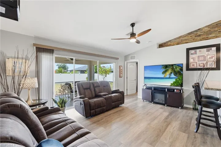 Spacious living area featuring wood-finish flooring, vaulted ceilings, and an exposed architectural beam with stone veneer