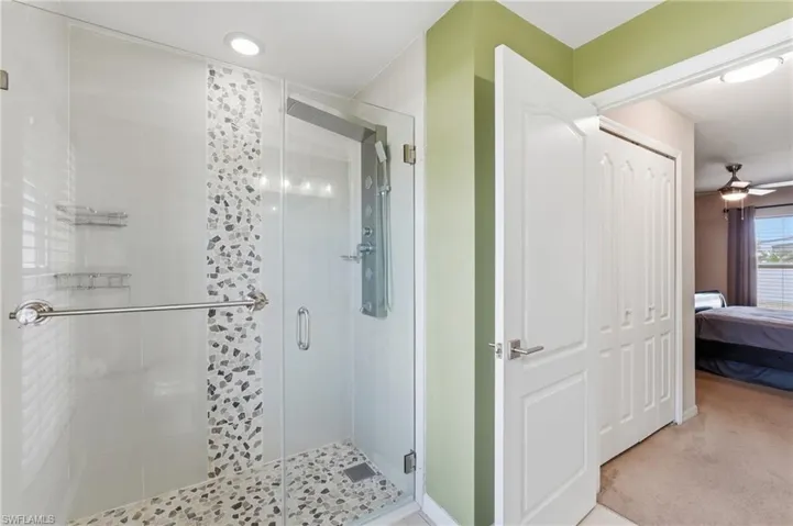 Glass-enclosed shower with a mosaic tile accent strip and river rock floor