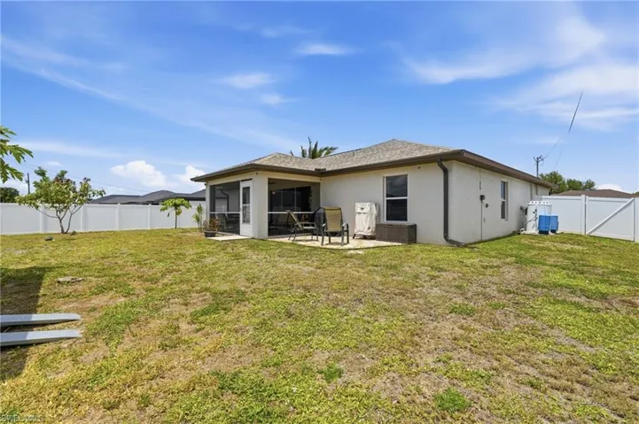 Rear exterior featuring a screened patio with a concrete slab, a white vinyl privacy fence, and a spacious lawn area