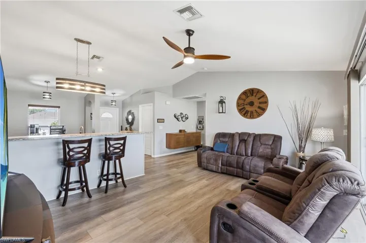 Open-concept living area featuring wood-finish flooring, a vaulted ceiling, and a ceiling fan with integrated lighting