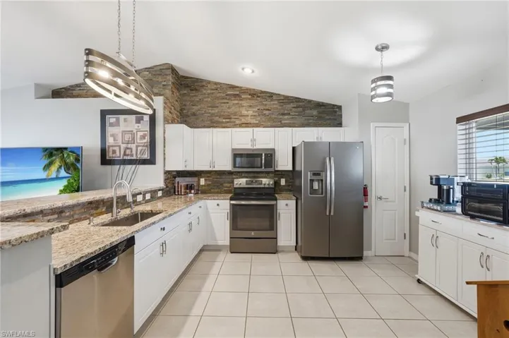 Bright kitchen featuring white cabinetry, granite countertops, tile flooring, stainless steel appliances, and a unique stacked stone accent wall