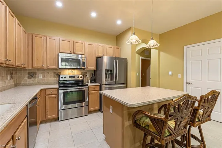 Kitchen featuring stainless steel appliances, decorative light fixtures, decorative backsplash, a kitchen island, and arched walkways