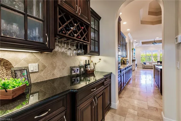 Bar featuring crown molding, backsplash, dark brown cabinetry, ceiling fan, and light tile floors