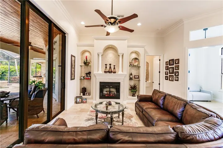 Tiled living room featuring crown molding, a large fireplace, and ceiling fan