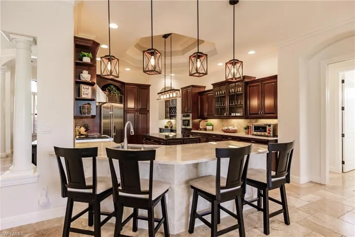 Kitchen featuring a spacious island, backsplash, appliances with stainless steel finishes, decorative columns, and pendant lighting