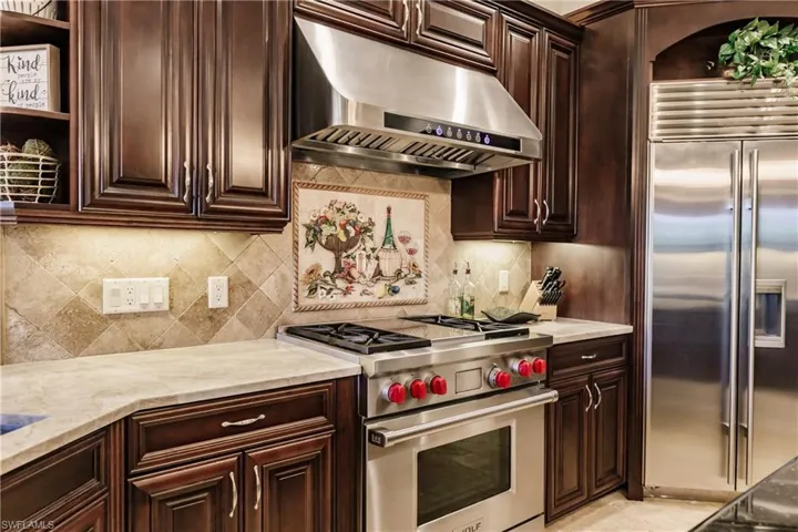 Kitchen with backsplash, light stone counters, wall chimney exhaust hood, and premium appliances