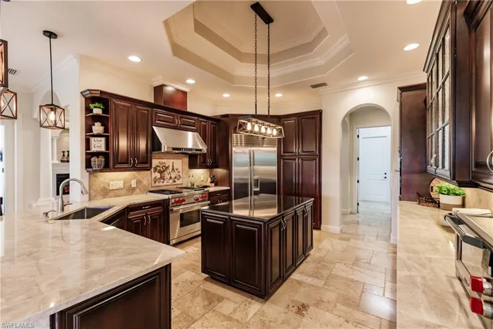 Kitchen featuring tasteful backsplash, light stone counters, high end appliances, sink, and ornamental molding