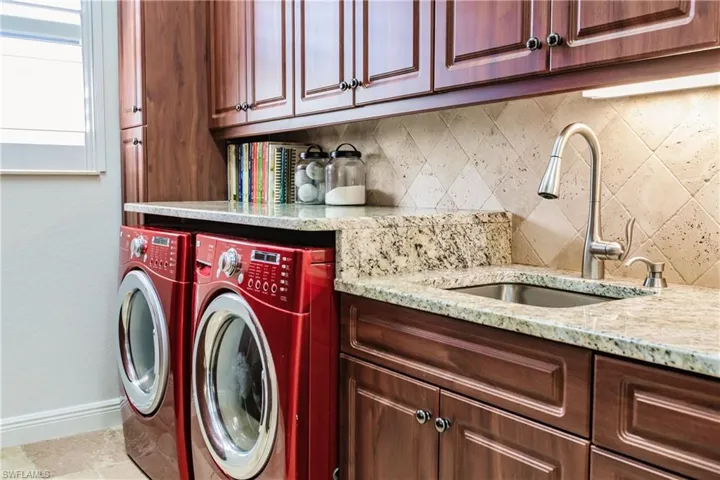 Clothes washing area with sink, washing machine and clothes dryer, light tile floors, and cabinets
