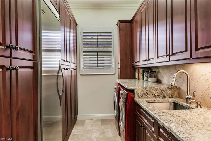 Kitchen featuring light stone counters, light tile flooring, washing machine and clothes dryer, backsplash, and sink