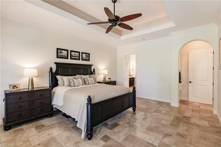 Tiled bedroom featuring ceiling fan, ensuite bathroom, a tray ceiling, and ornamental molding