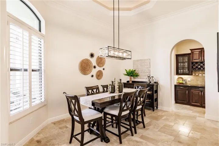 Tiled dining space with a wealth of natural light, a notable chandelier, ornamental molding, and a raised ceiling