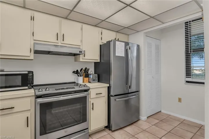 Kitchen featuring stainless steel appliances, under cabinet range hood, a paneled ceiling, and light countertops